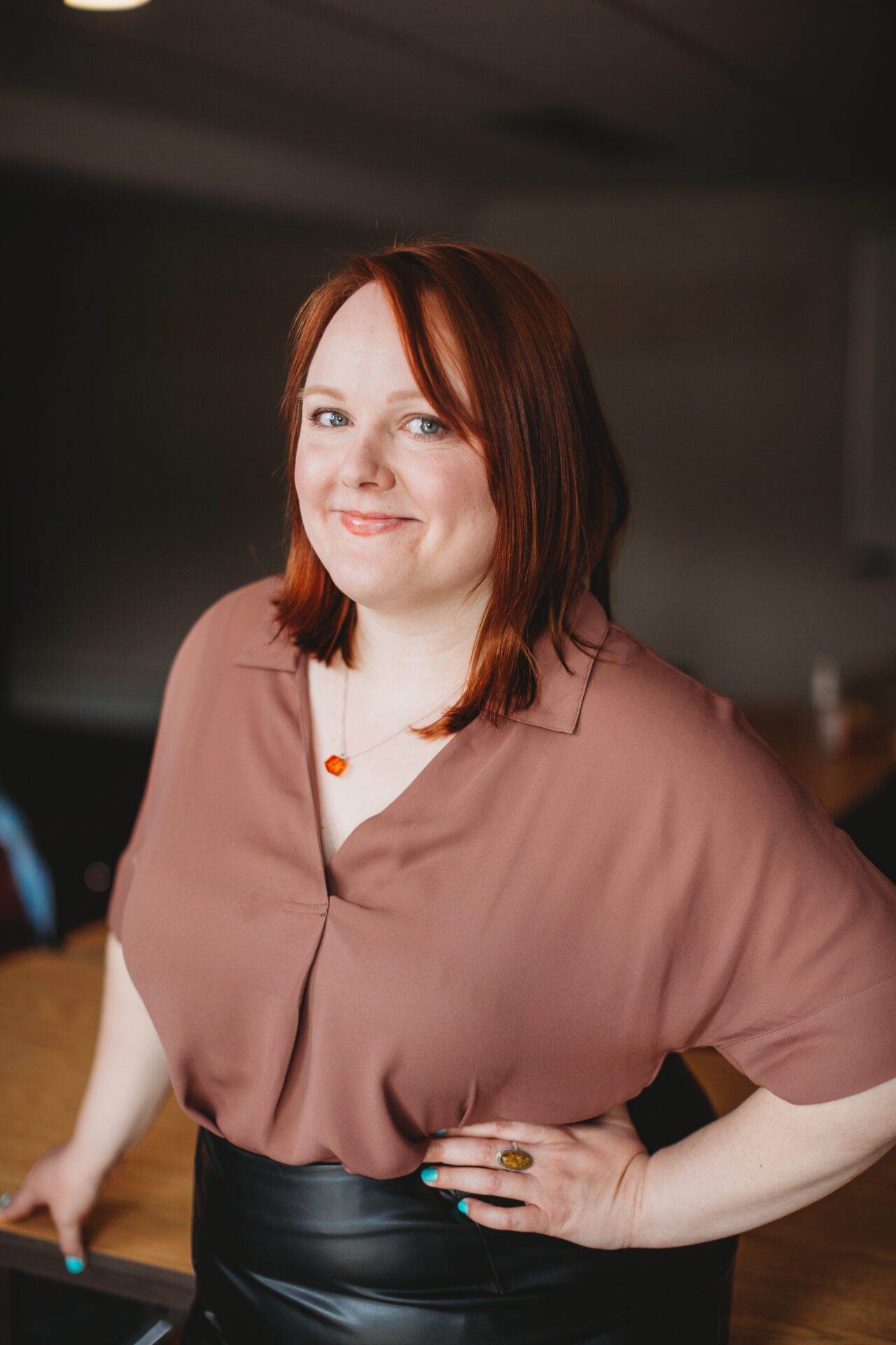 Amy stands smiling with one hand on her hip in a boardroom.